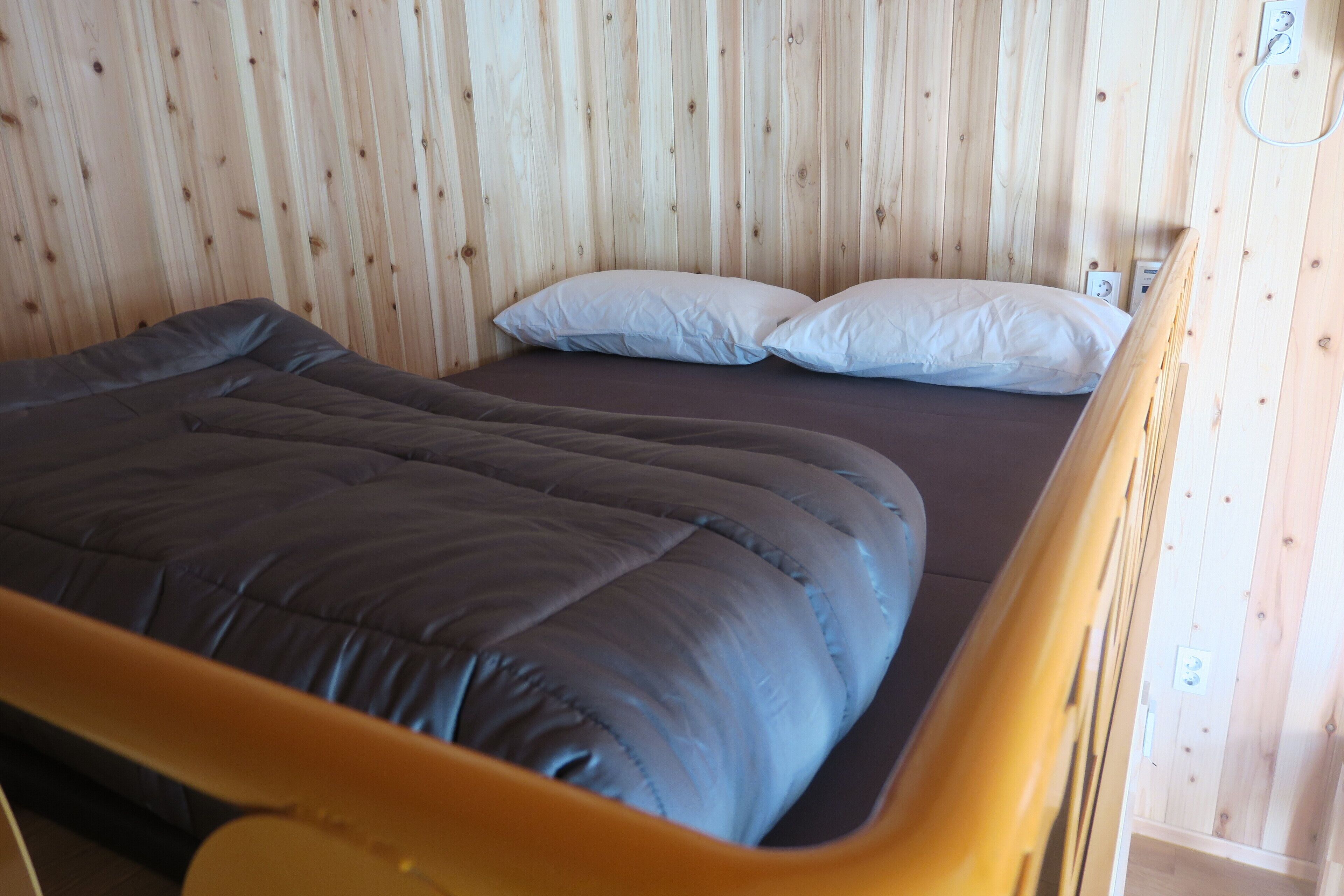 A bed with a dark-colored mattress and two white pillows in a room with wooden walls.