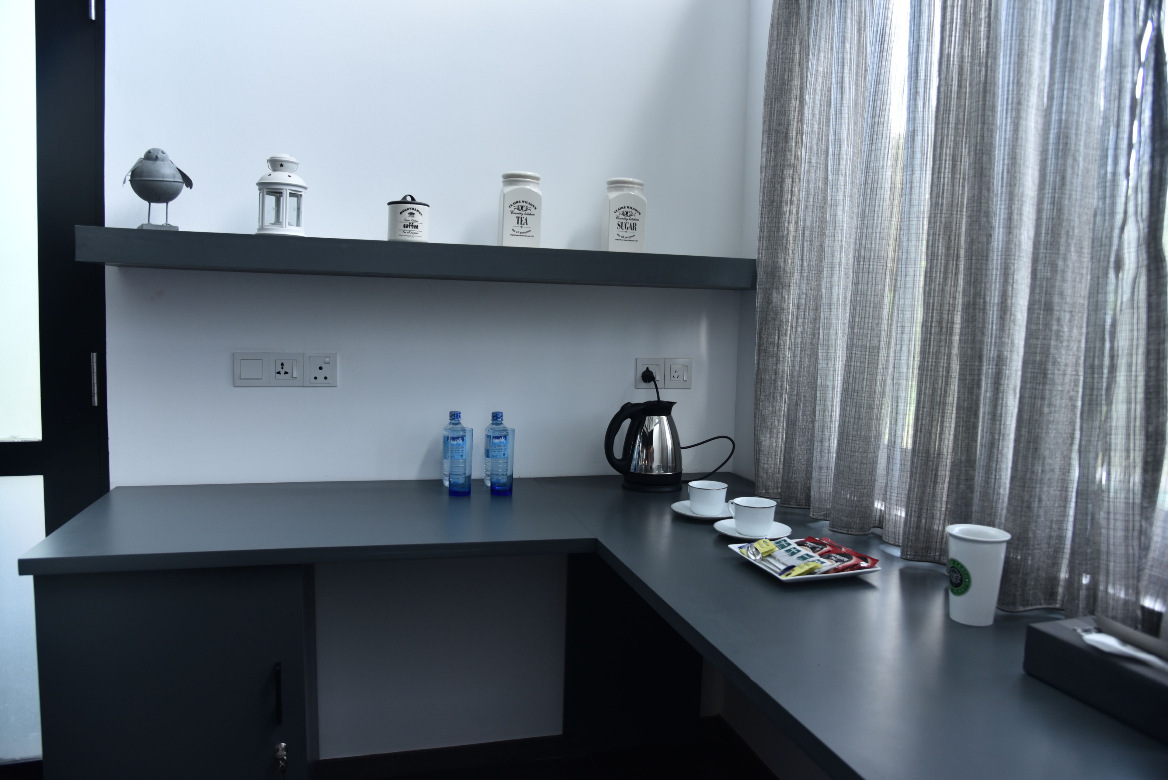 A modern kitchen with a dark countertop, a kettle, cups, and jars labeled tea and sugar.