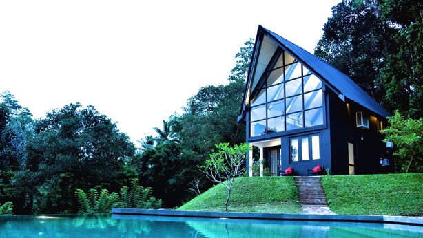 A modern house with a large glass facade, a swimming pool, and lush greenery surrounding it. - The Country House (Galle)