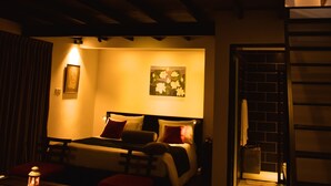 A dimly lit room with a bed, a small table with a lantern, and a staircase leading to an upper level. - The Country House (Galle)