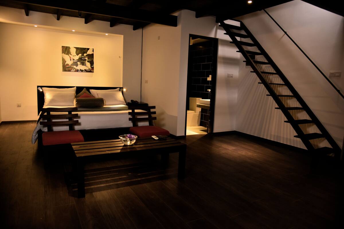 A modern bedroom with a bed, a bench, a staircase, and a wall-mounted shelf.