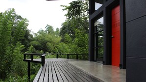 A wooden deck with a black railing, leading to a building with a red door. - The Country House (Galle)