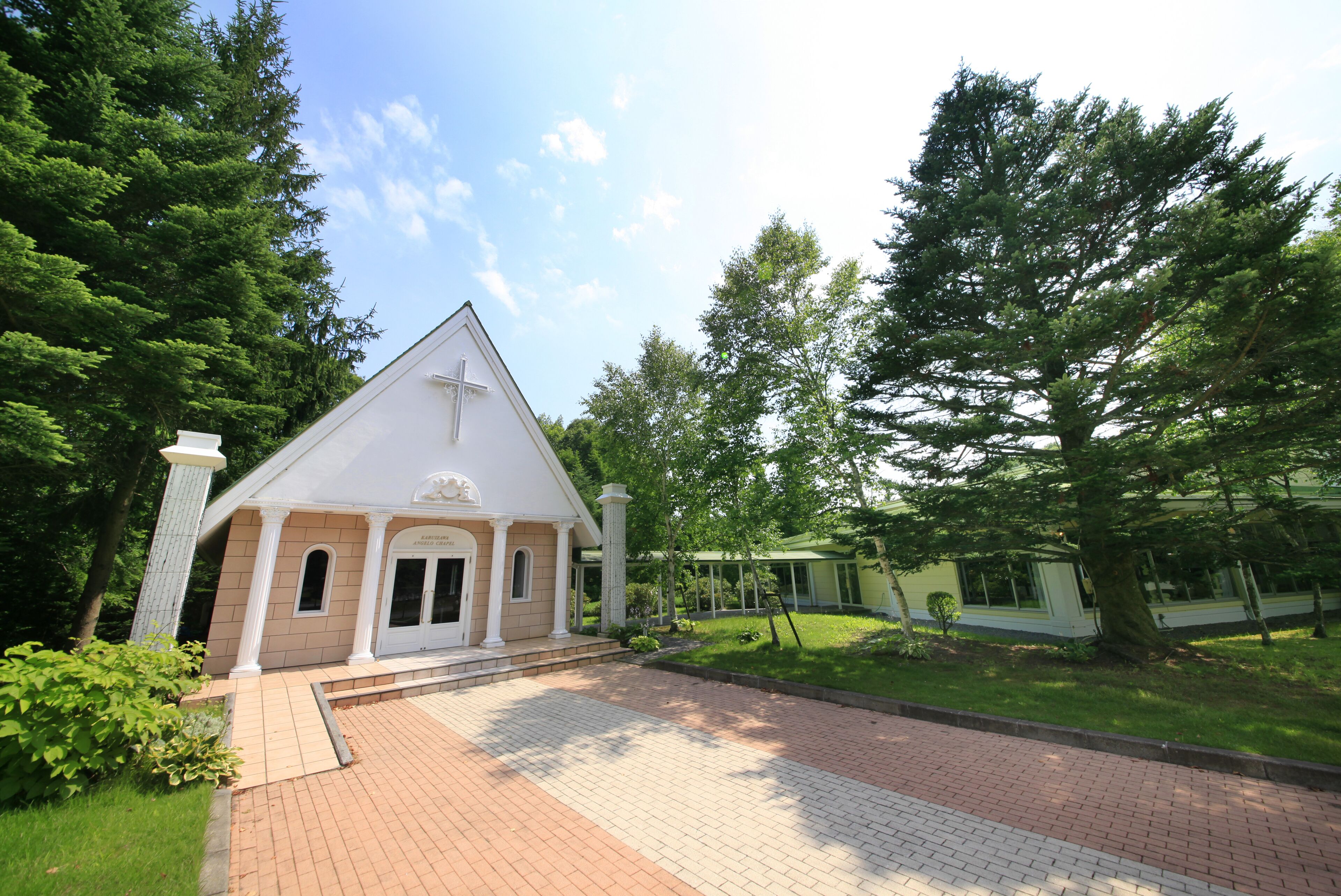 A church with a white facade, a cross on the front, and a brick pathway leading to it.
