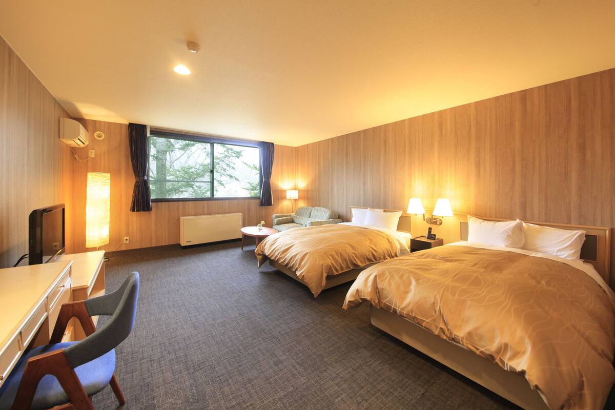 Ett hotellrum med två sängar, ett skrivbord, en stol, en TV och ett fönster med gardiner.