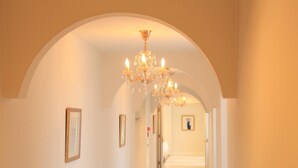 A hallway with a chandelier, framed pictures on the walls, and a tiled floor.