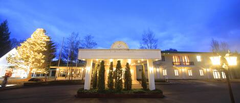 A hotel entrance with a covered area, a Christmas tree, and a well-lit facade.