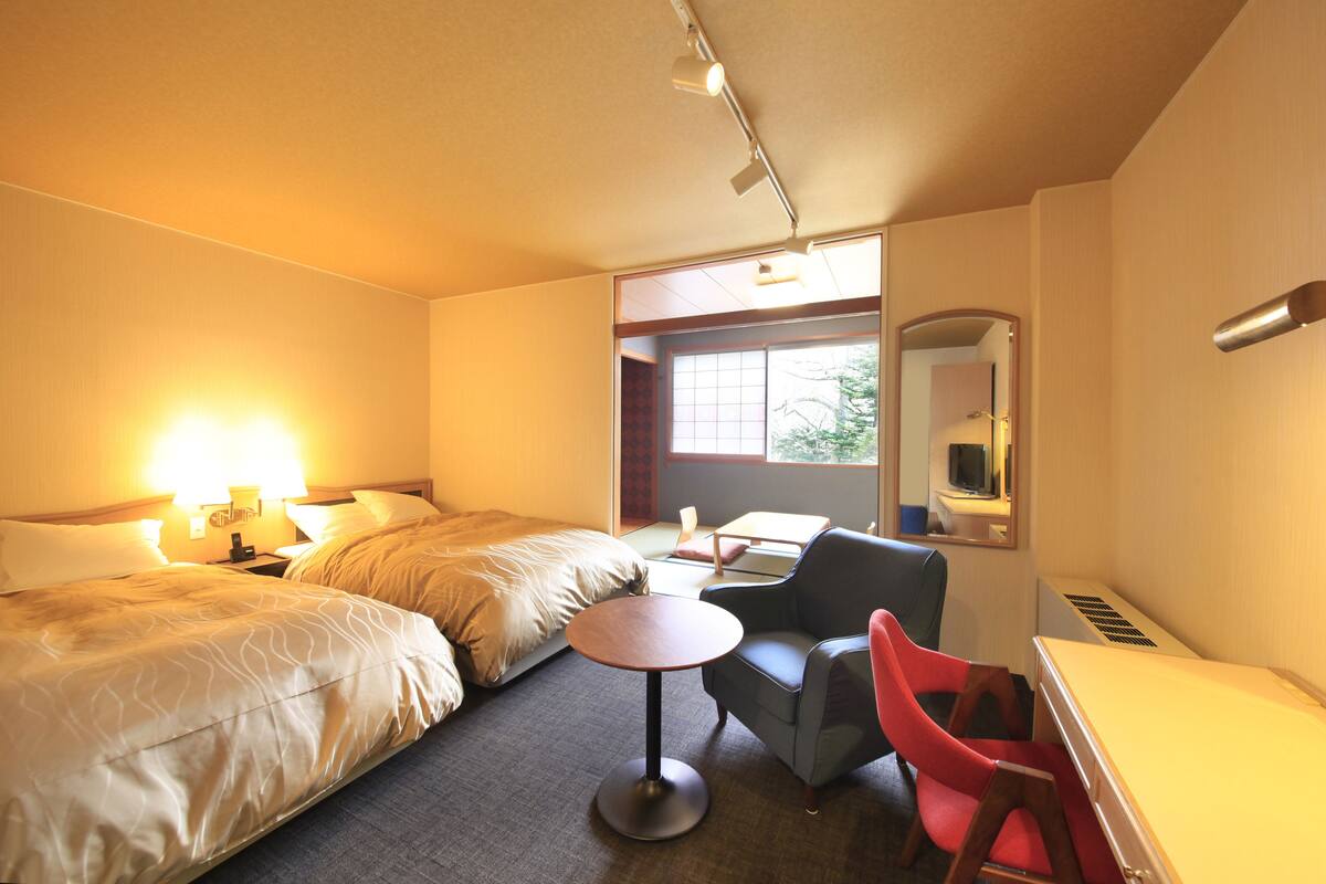 Ett hotellrum med två sängar, ett litet runt bord, en röd stol, ett skrivbord och en spegel.