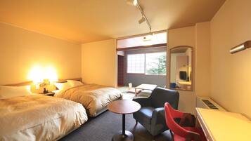 A hotel room with two beds, a small round table, a red chair, a desk, and a mirror.