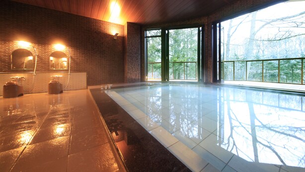 A spacious indoor swimming pool with a wooden ceiling and large windows offering a view of trees.