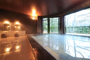 A spacious indoor swimming pool with a wooden ceiling and large windows offering a view of trees.