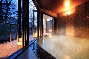 Un interior moderno con puertas de cristal amplias que dan a un espacio exterior, suelo de baldosas y una pared de ladrillo con una lámpara.
