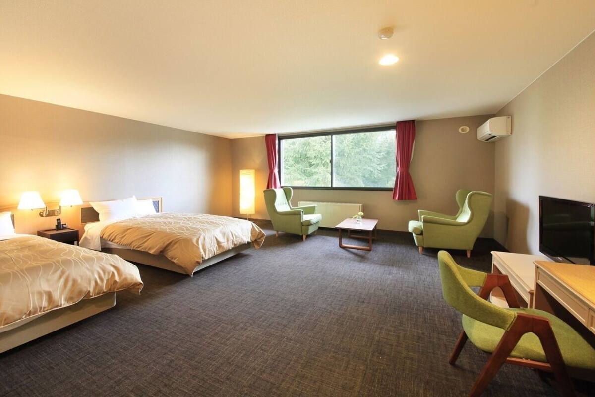 Ett hotellrum med två sängar, ett skrivbord, en stol, en TV och ett fönster med gardiner.