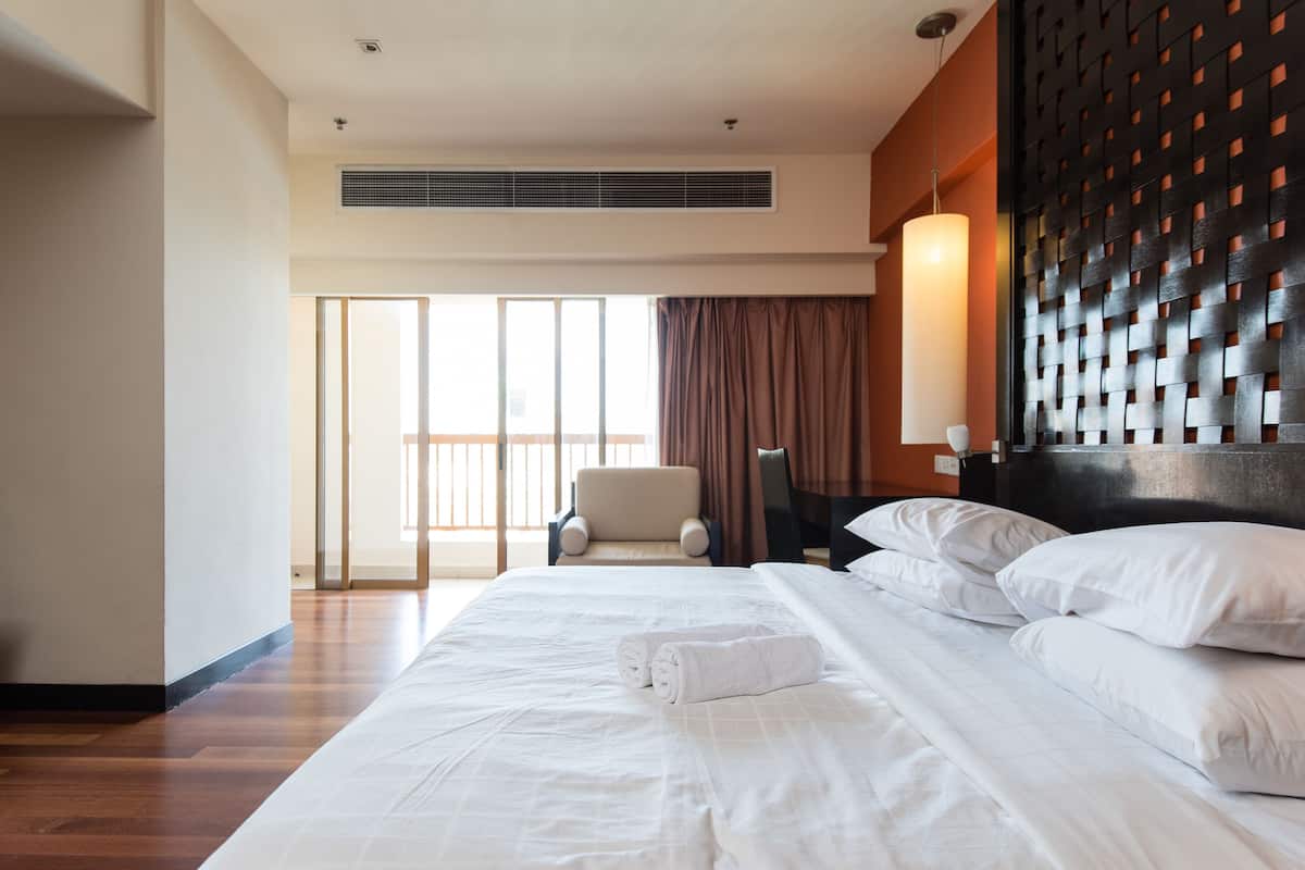 A hotel room with a large bed, a chair, a desk, and a view of the outside through a large window.