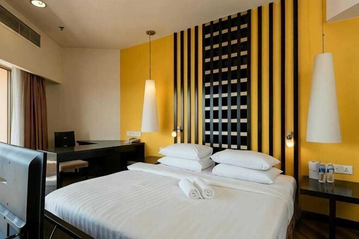 A hotel room with a bed, bedside table, desk, and lamp.