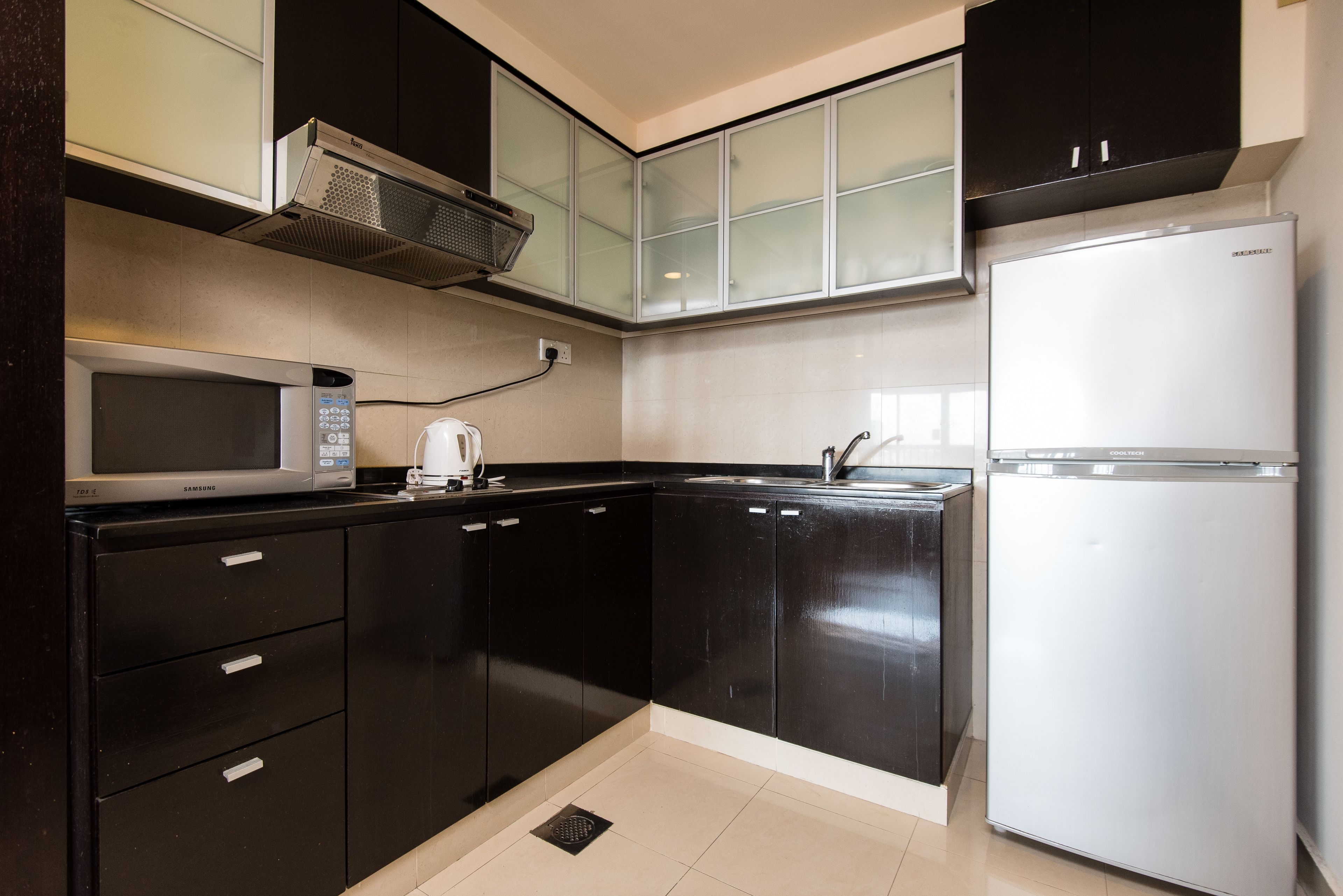Une cuisine moderne avec des meubles de rangement noirs, un réfrigérateur en acier inoxydable, un four à micro-ondes et un four encastré.