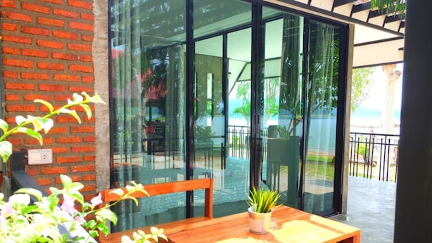 Une table en bois sur laquelle est posée une plante en pot, une porte vitrée donnant sur un espace extérieur avec vue sur une plage et un mur en briques.