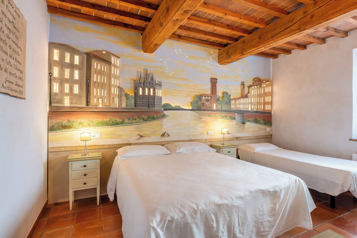 A hotel room with two beds, a mural of a cityscape, wooden ceiling beams, and a tiled floor.