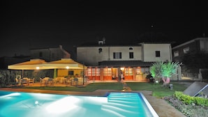 A swimming pool with a sun lounger area, a patio with outdoor furniture, and a building with a tiled roof in the background. - Villa Maria (Vicopisano)
