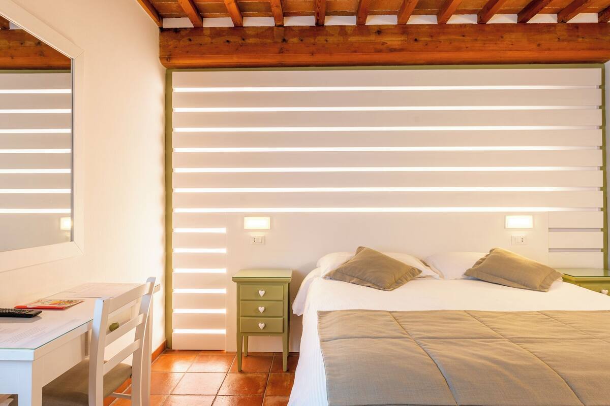 A bedroom with a bed, bedside tables, a desk, and a window.