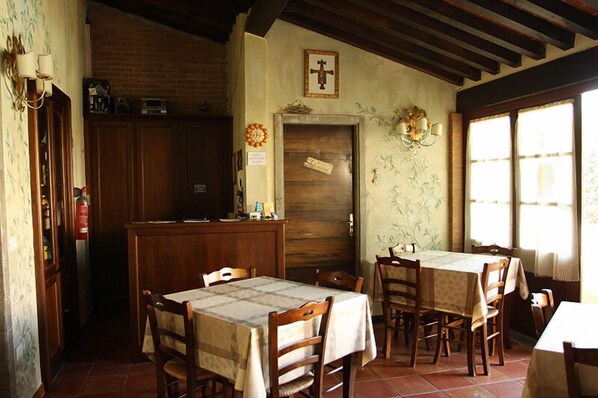 Un comedor con mesas y sillas de madera, pared de ladrillo y puerta de madera con una cruz encima.
