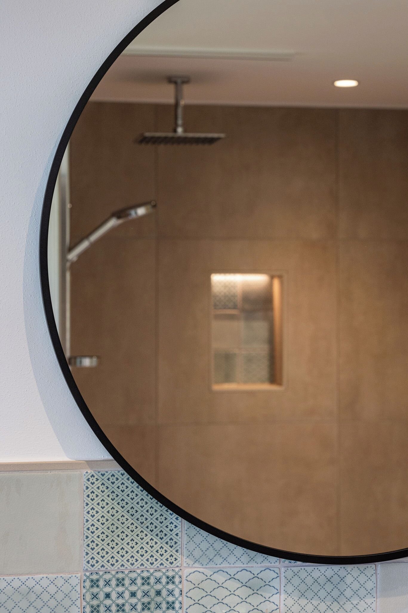 A circular mirror reflecting a shower area with a glass enclosure and a metal showerhead.