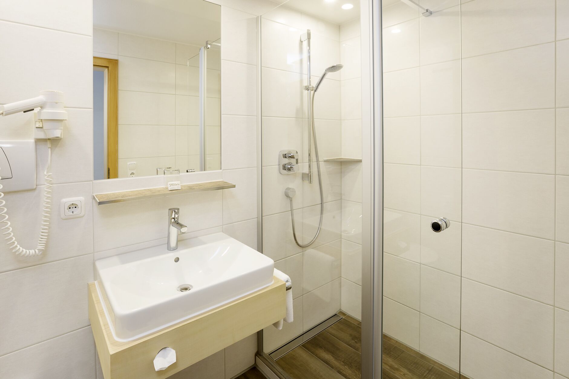 A modern bathroom with a white sink, mirror, and shower.