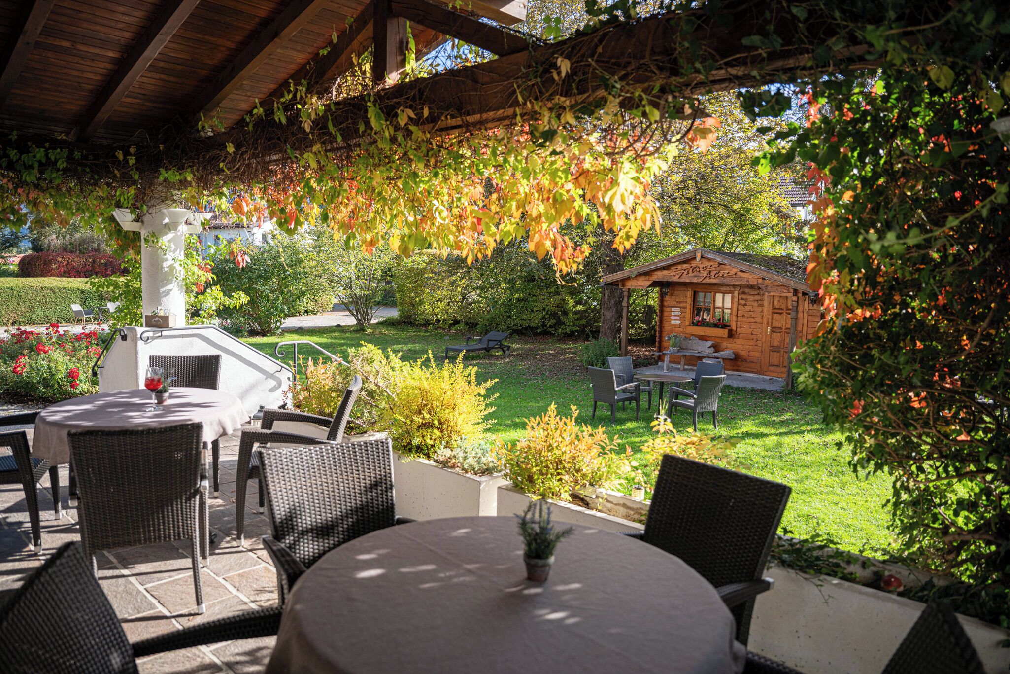 An outdoor patio with wicker furniture, a small wooden structure, and a garden with various plants and a lawn.