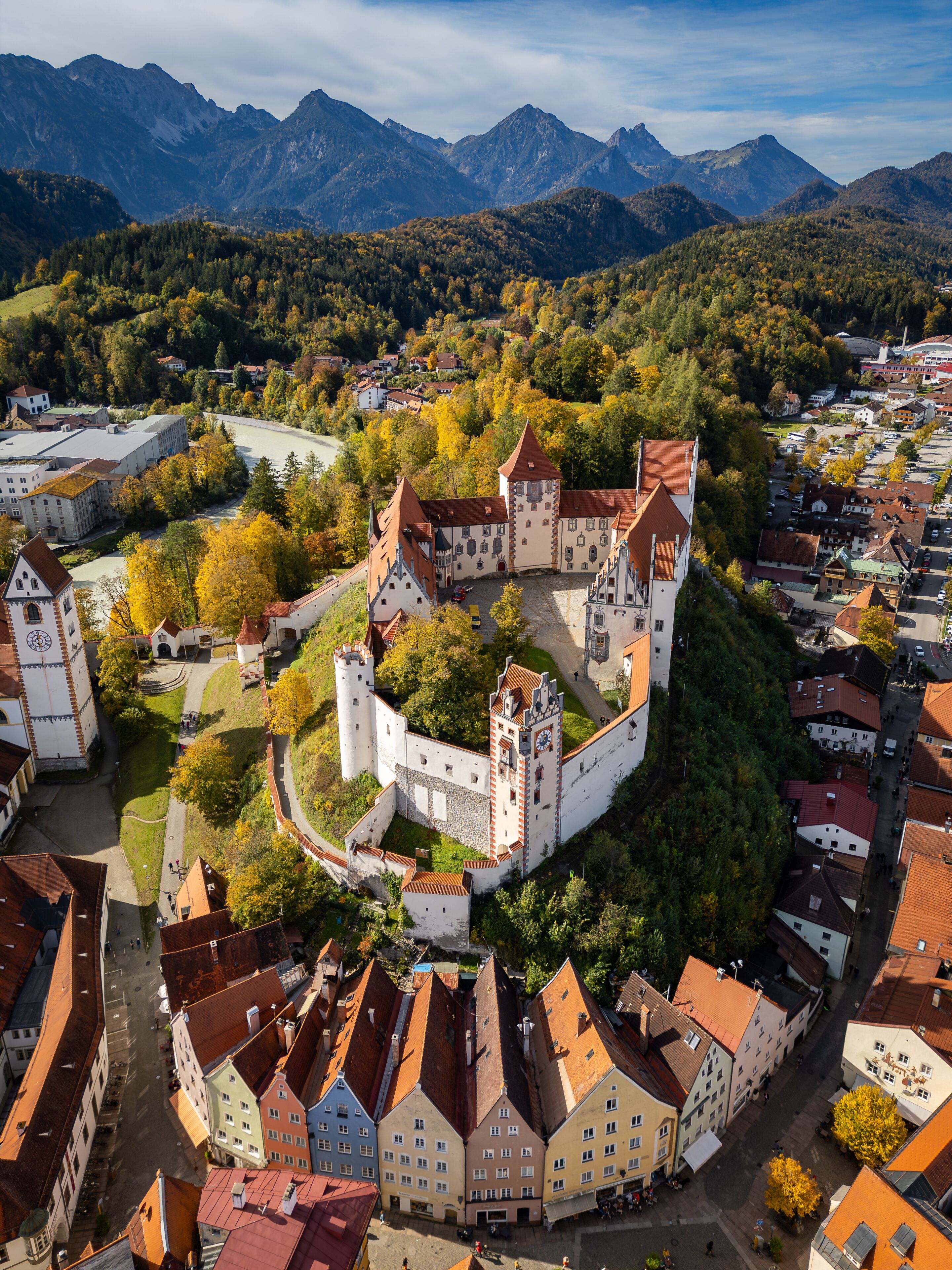 An aerial view of a historic castle surrounded by a walled town, with mountains in the background.