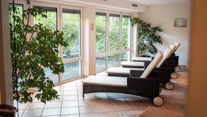 A sunlit room with large windows, a tiled floor, and several lounge chairs. - Hotel Filser (Fuessen)