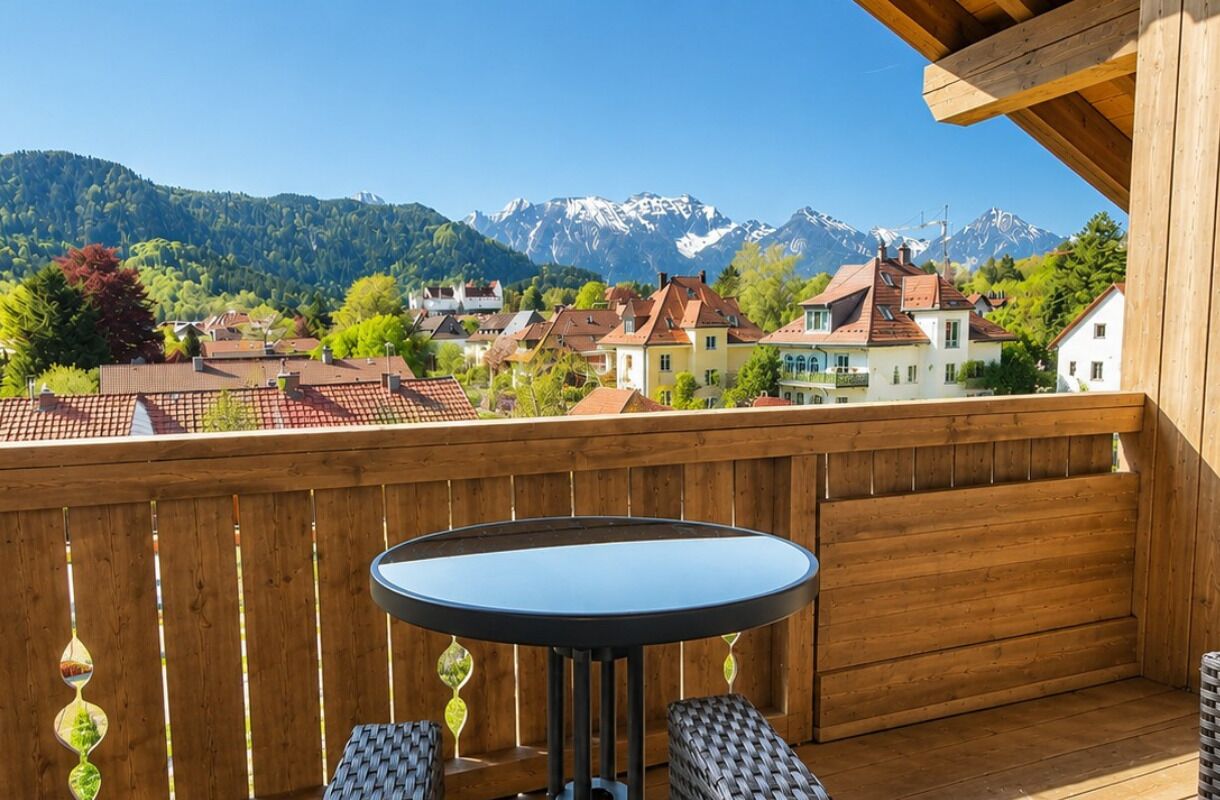 Ein Balkon mit Tisch und Stühlen, mit Blick auf ein Dorf mit Häusern und Bergen.
