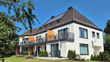 Una casa moderna de dos pisos con un balcón, paneles solares y un jardín bien cuidado.