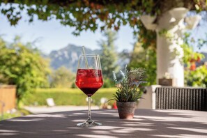Una copa de vino tinto sobre una mesa al aire libre, con una planta en maceta y montañas al fondo.