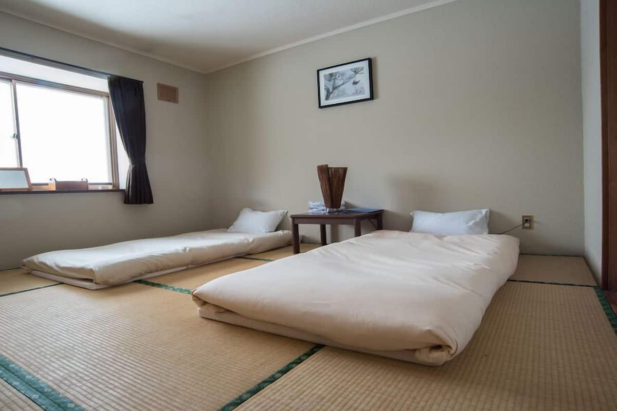 A hotel room with two beds, a small table, a window with curtains, and a framed picture on the wall.