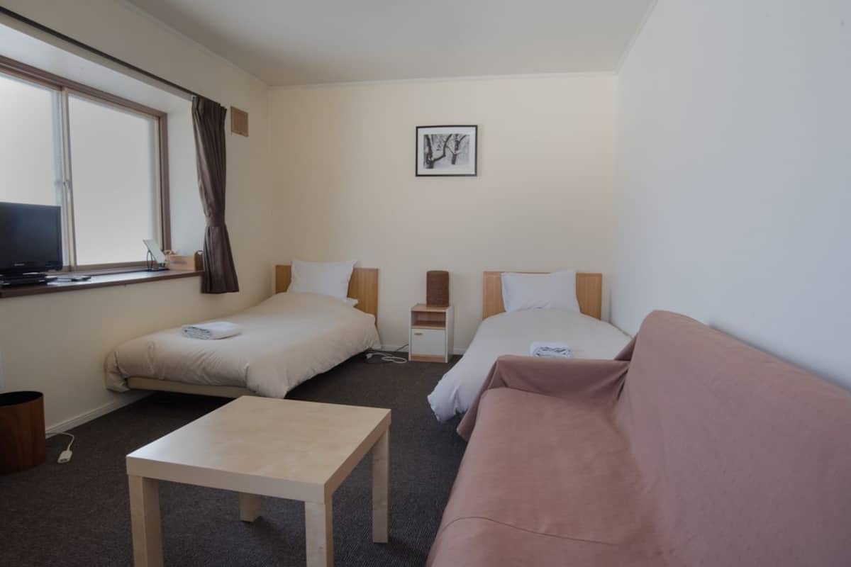 A hotel room with two single beds, a sofa, a small table, and a TV on a desk.