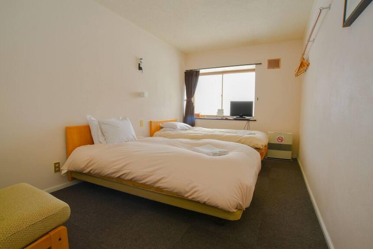 A hotel room with two beds, a window with curtains, a television, and an air conditioning unit.