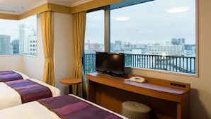 A hotel room with two beds, a desk with a TV, a phone, and a window with a city view.