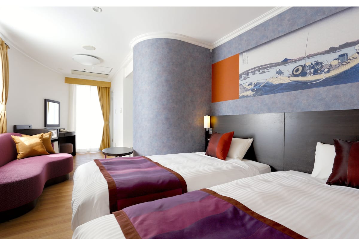 A hotel room with two beds, a desk, a chair, and a large painting on the wall.