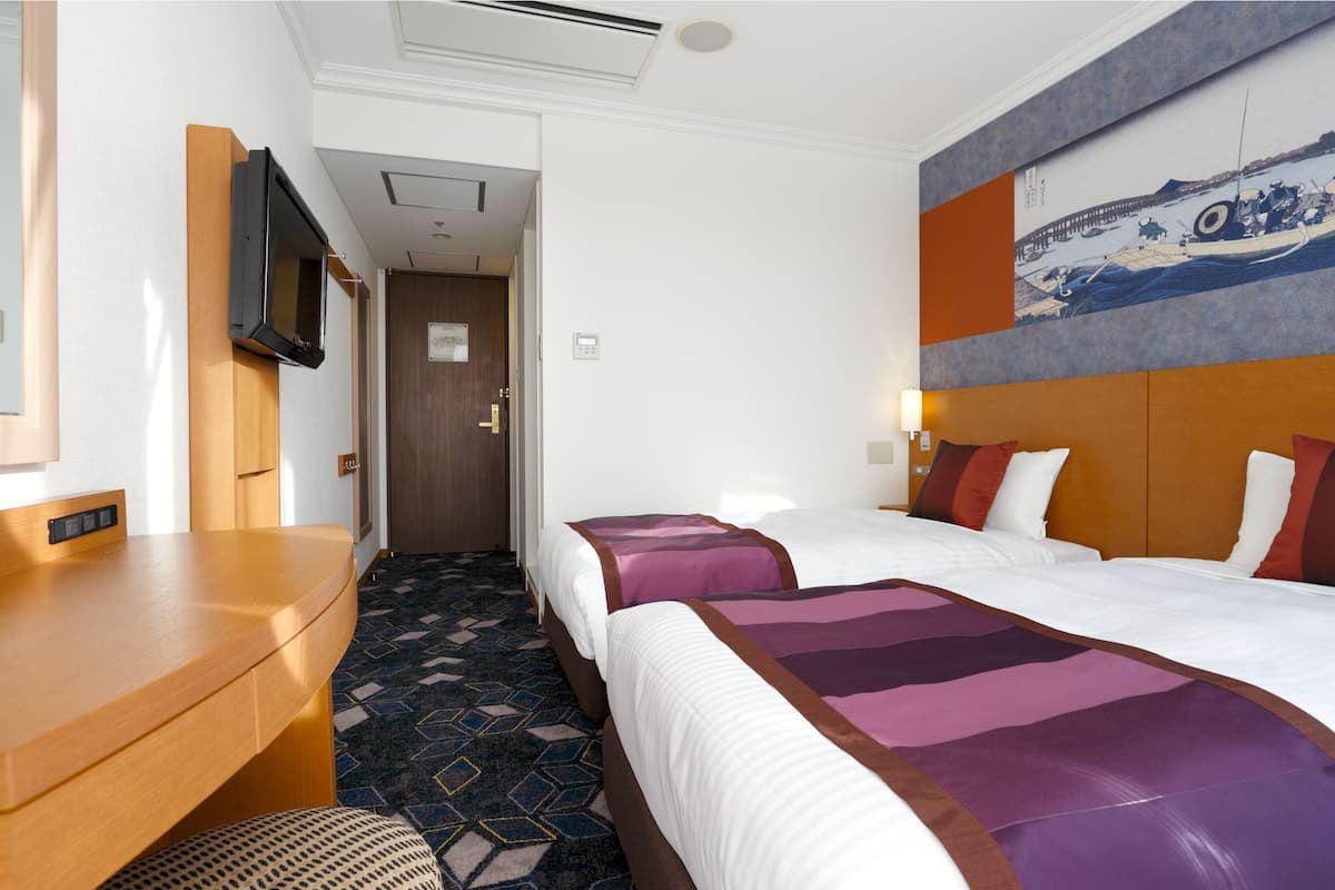 A hotel room with a bed, a desk, a television, and a painting on the wall.