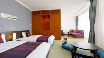 A hotel room with two beds, a sofa, a small table, and a view of the outdoors.