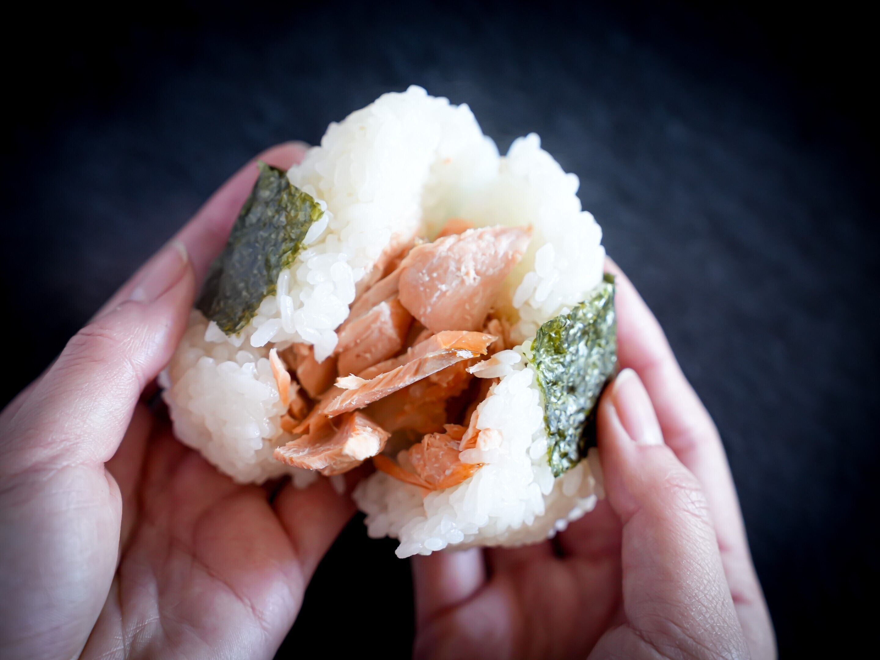 Una mano sostiene un rollo de sushi de arroz, salmón y alga marina.