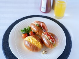 A plate with two hot dogs, one with a visible egg and the other with lettuce and tomato, accompanied by cherry tomatoes and a small salad.