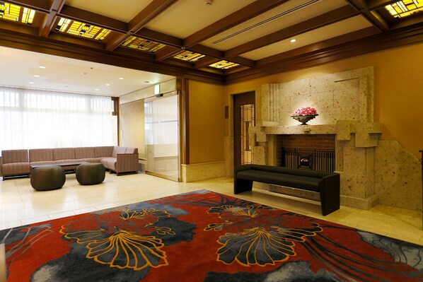 A spacious lobby with a large red floral carpet, a fireplace, and a seating area with sofas and ottomans.