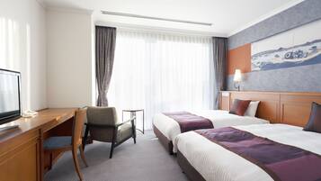 A hotel room with a wooden desk, two beds, a TV, and a painting on the wall.