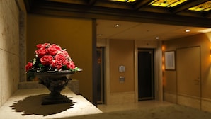 A reception area with a vase of red flowers on a counter, a tiled floor, and a hallway with doors. - Ryogoku View Hotel (Tokyo)