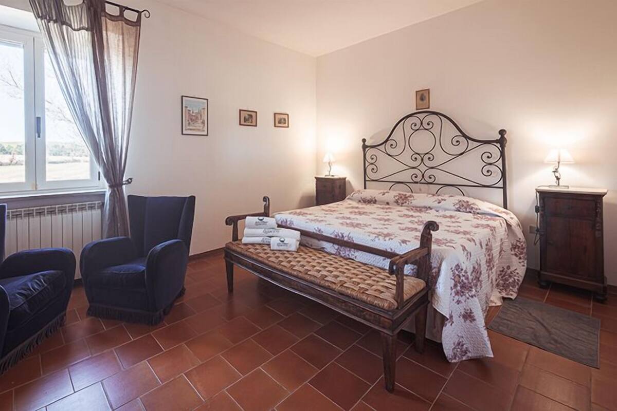 A bedroom with a bed, two armchairs, a small table, and a window with curtains.