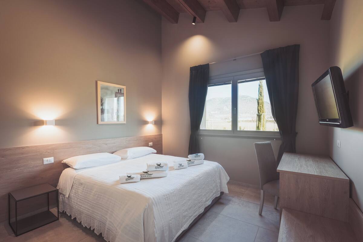 A bedroom with a bed, bedside tables, a desk, and a window with curtains.