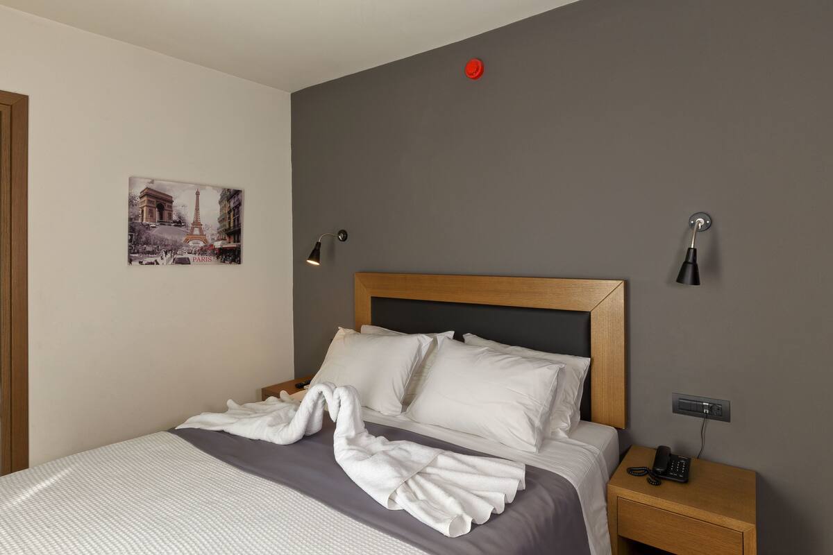 Cama bem arrumada com lençóis brancos, cabeceira de madeira e mesa de cabeceira com um telefone.