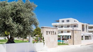 A modern hotel with a white facade, a large tree in front, and a sign that reads "EVITA". - Evita Resort (Rhodes)