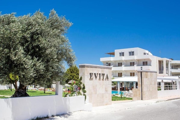 Un hotel moderno con fachada blanca, un gran árbol en frente y un letrero que dice "EVITA".