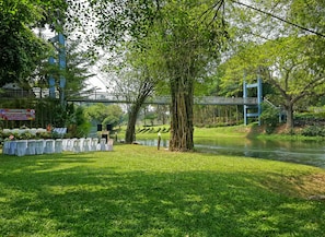 A riverside park with a bridge, grassy areas, and a row of white chairs.